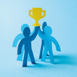 Four blue people made from cardboard holding award on blue background