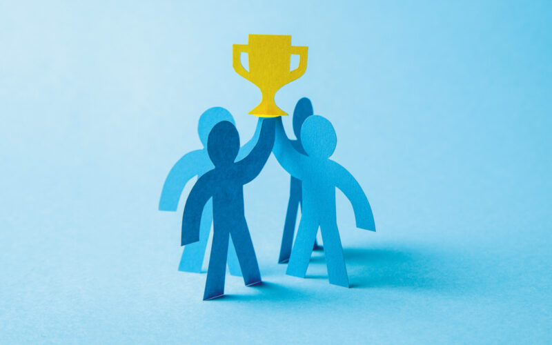 Four blue people made from cardboard holding award on blue background