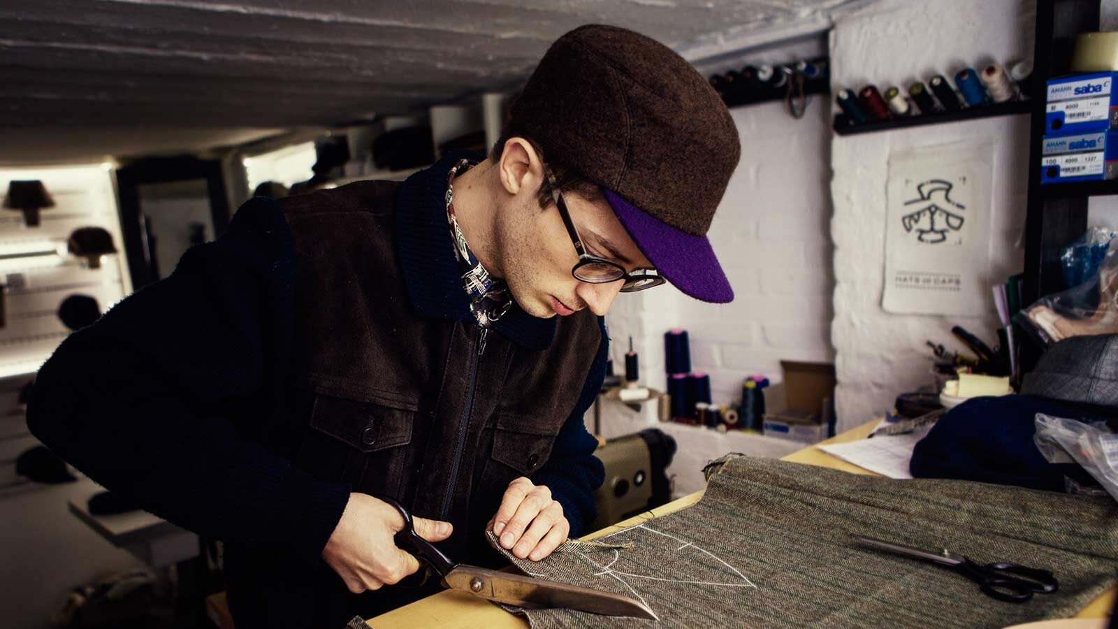 The capmaker Silas Gärtner cutting fabric with a scissor